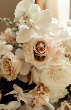 Wedding rings nestled in delicate blush roses and white orchids creating an elegant bridal arrangement.