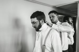 Two people preparing for a formal event with the one in front wearing suspenders and a white dress shirt.