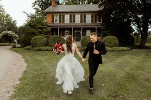 Newlyweds run joyfully on the lawn of a charming historic brick house with landscaped gardens.