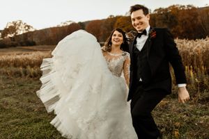 Joyful newlyweds walking together in an autumn field with the bride's dress flowing in the wind.