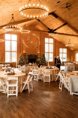 Rustic wedding reception venue with wooden walls, round tables and elegant chandelier lighting.