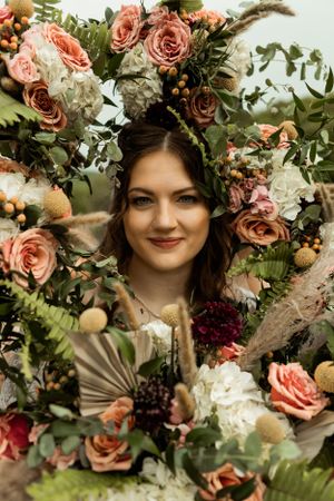 Artistic bridal portrait surrounded by lush floral arrangement with roses and greenery.