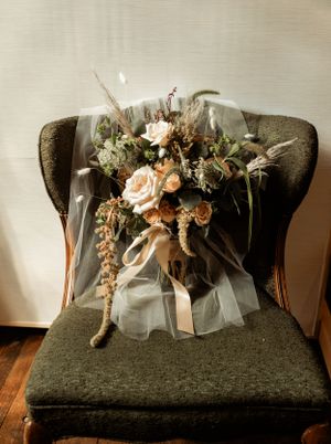A vintage wedding bouquet with peach roses rests elegantly on a dark green velvet armchair.