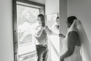 An emotional black and white candid moment shared by a window during wedding preparations.