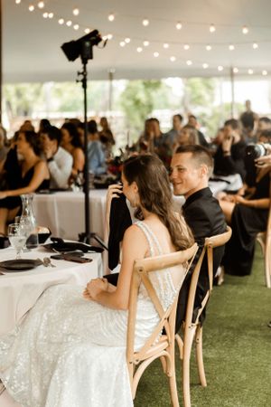 An elegant wedding reception scene showing the head table under twinkling lights in a tent venue.