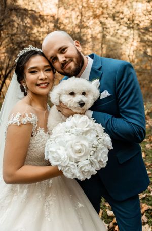 Wedding portrait with a couple and their white fluffy dog holding a bouquet of white roses.
