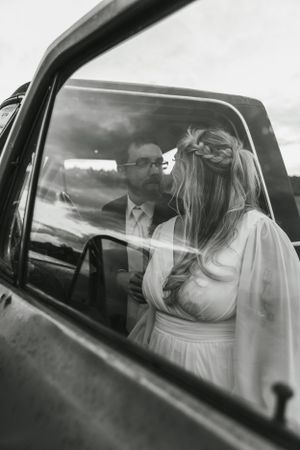Black and white photo of newlyweds sitting in vintage car after wedding ceremony.