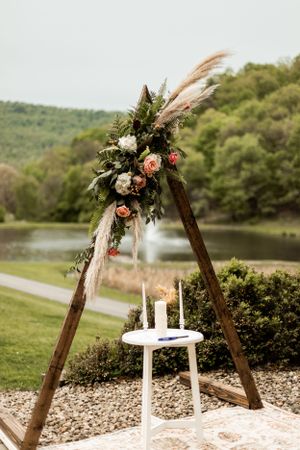 Rustic wooden arch decorated with florals and pampas grass with unity candle table.