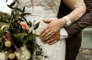 Close up of wedding details showing rings, bouquet and lace dress details.