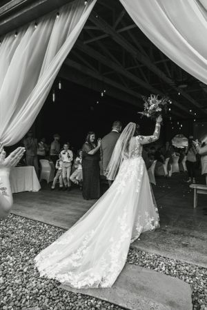 Bride in lace dress with long train throws her bouquet at wedding reception under draped fabric decor.