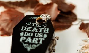 A gothic wedding ring holder with 'Till Death Do Us Part' engraving surrounded by autumn leaves.