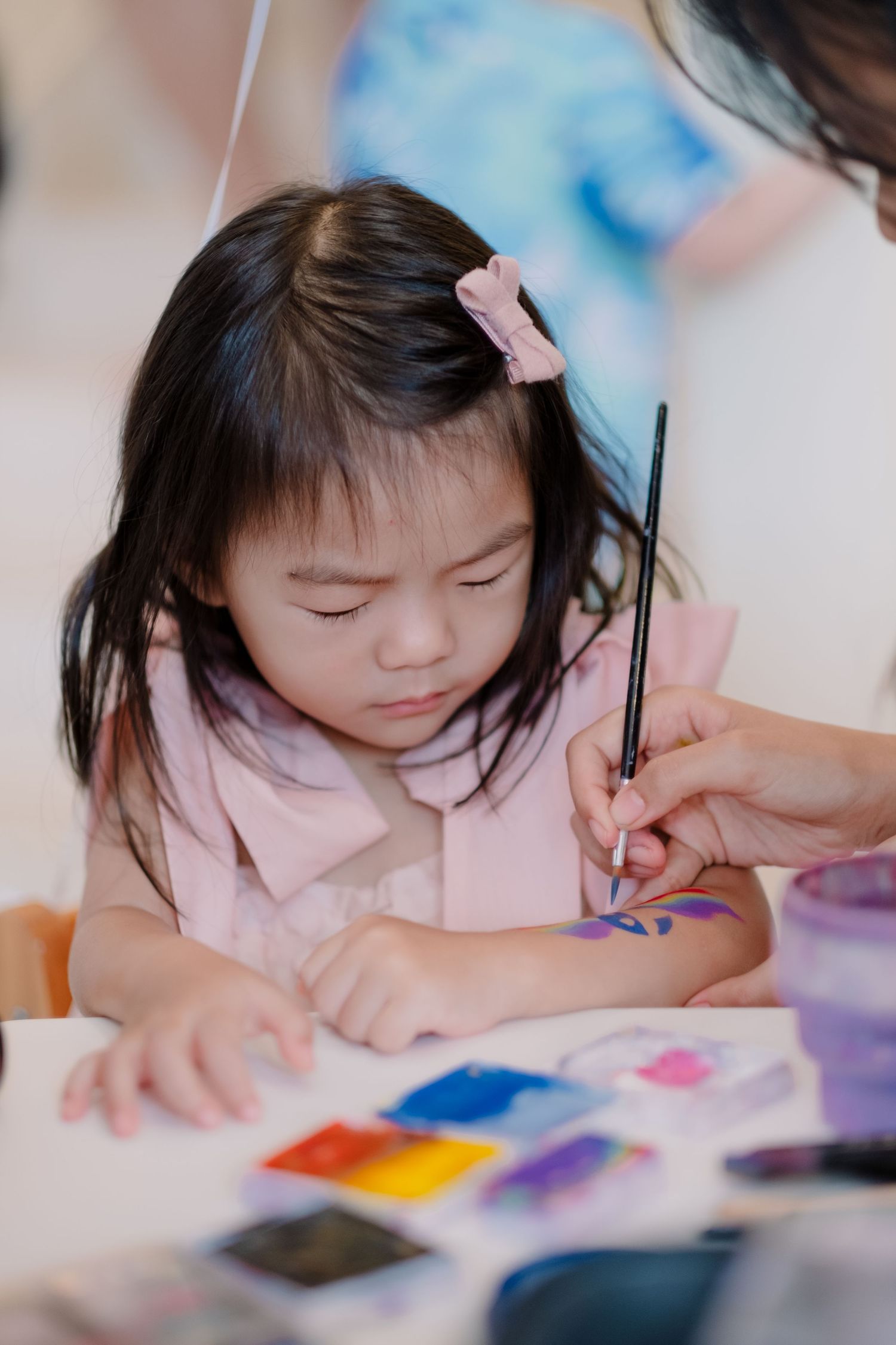 Young artist concentrating on painting with watercolors while wearing a pink hair clip.
