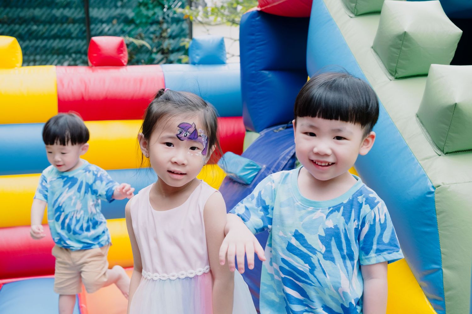 Children in tie-dye shirts playing on colorful inflatable bounce house.