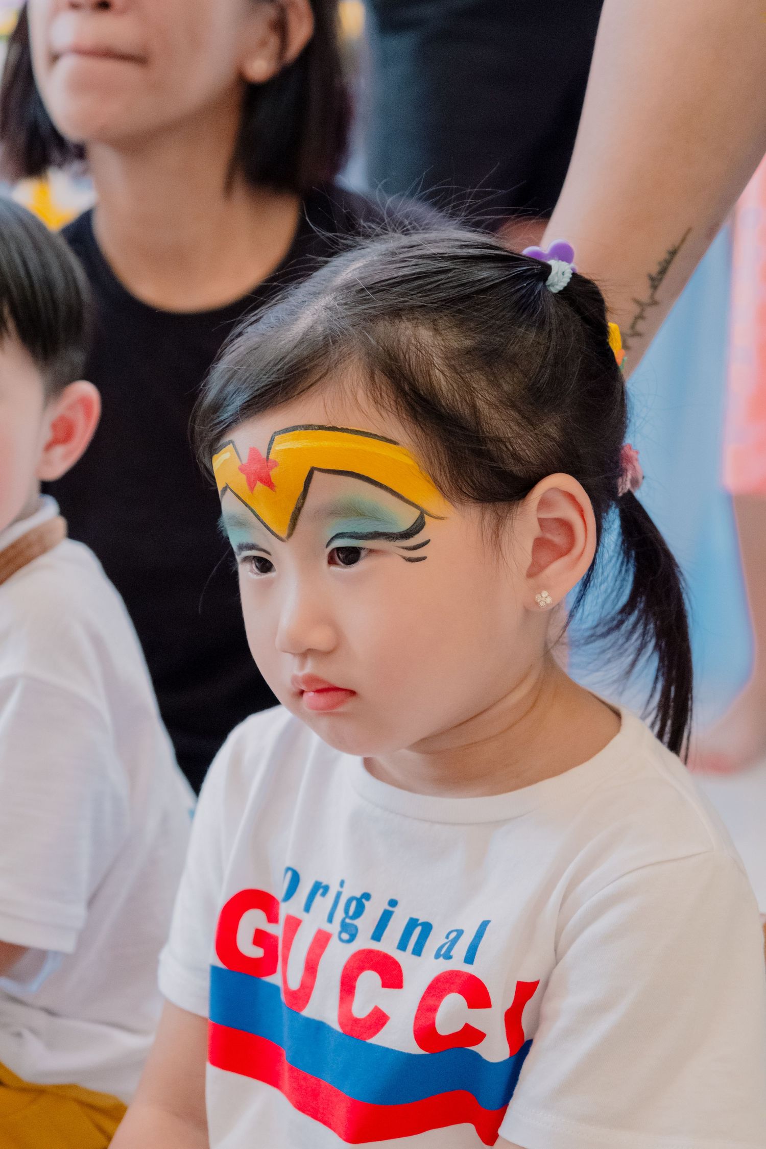 Young child wearing a white Gucci shirt with colorful face paint design at a party event.