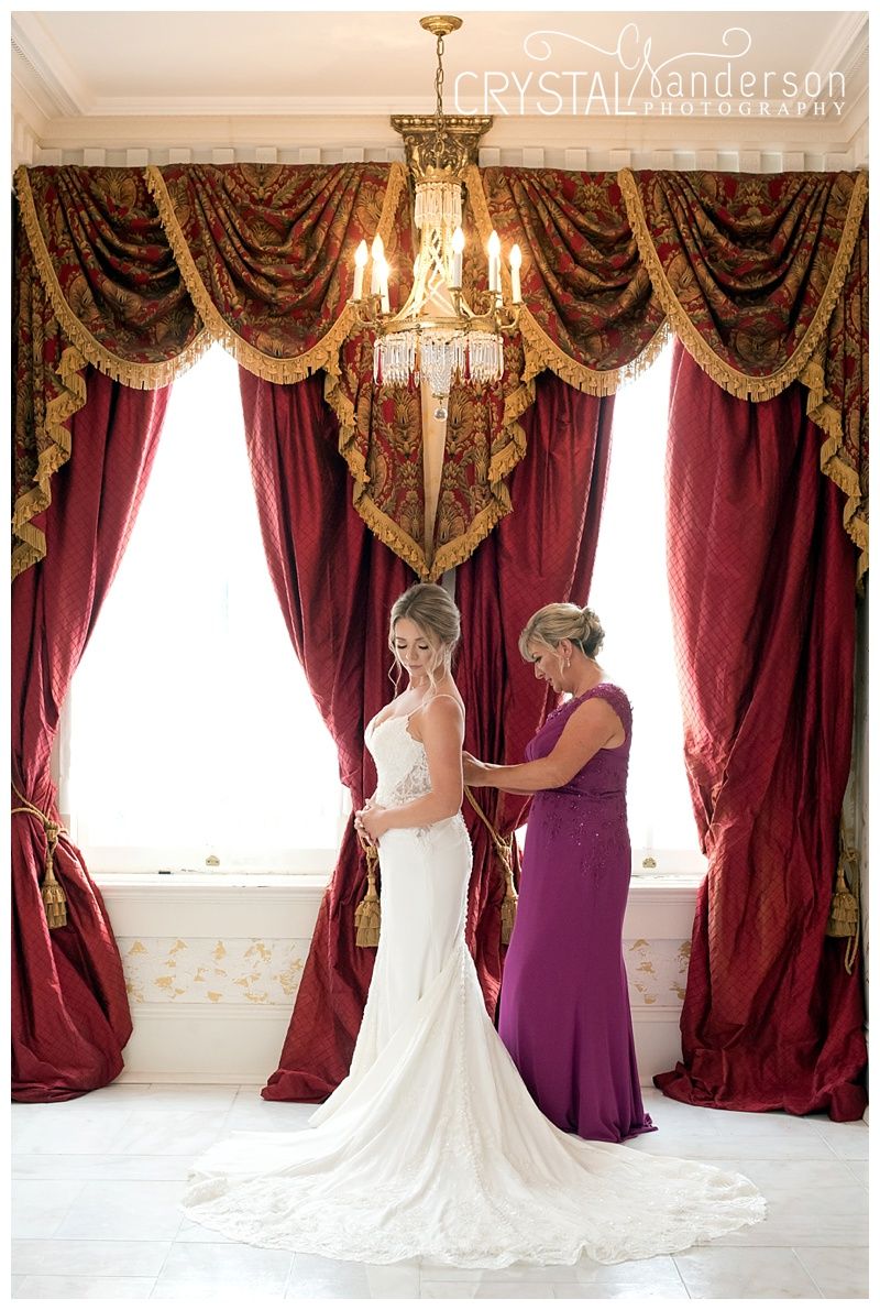 Wedding dress and purple bridesmaid gowns in elegant room with burgundy curtains.