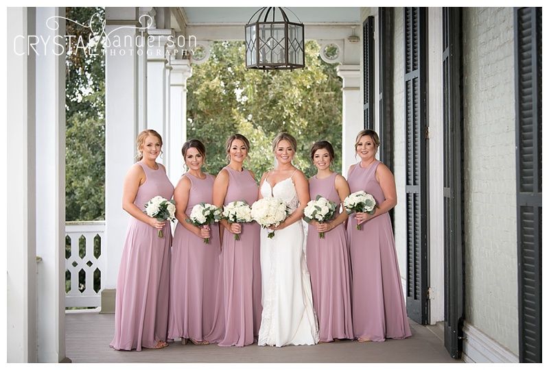 Wedding party poses along a classic white columned porch with bridesmaids in mauve dresses.