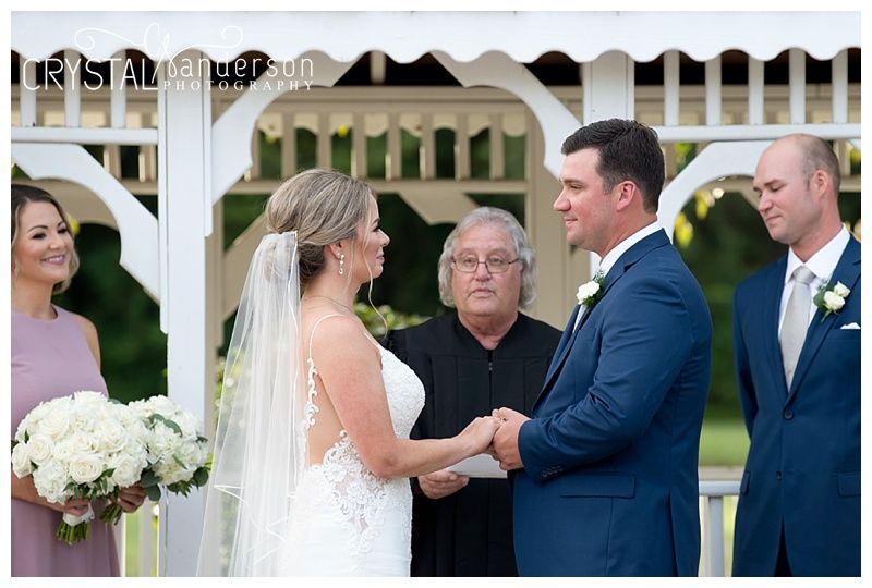 Wedding ceremony vows being exchanged under an ornate white gazebo.