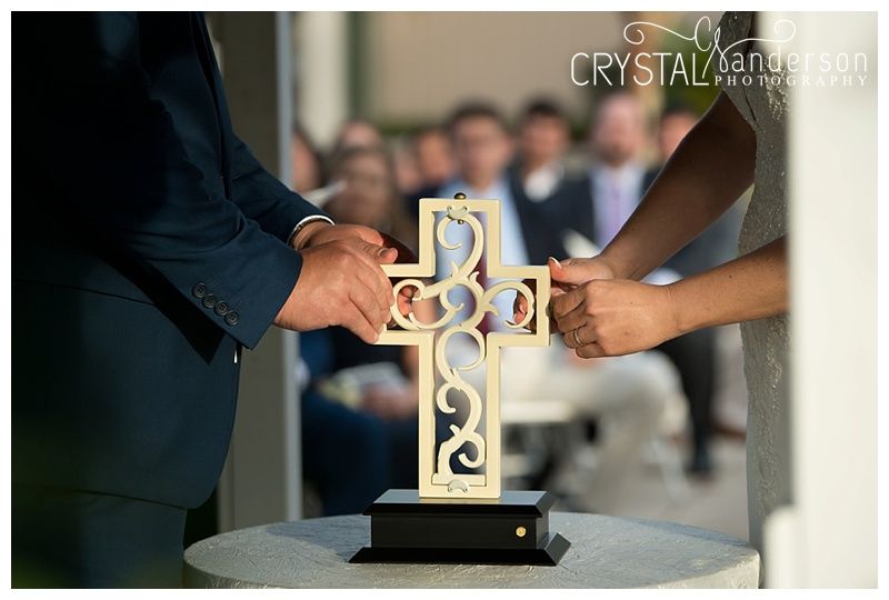 Hands joining together to hold a decorative unity cross during wedding ceremony.