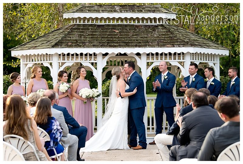 Wedding ceremony taking place in ornate white gazebo with guests seated on both sides.