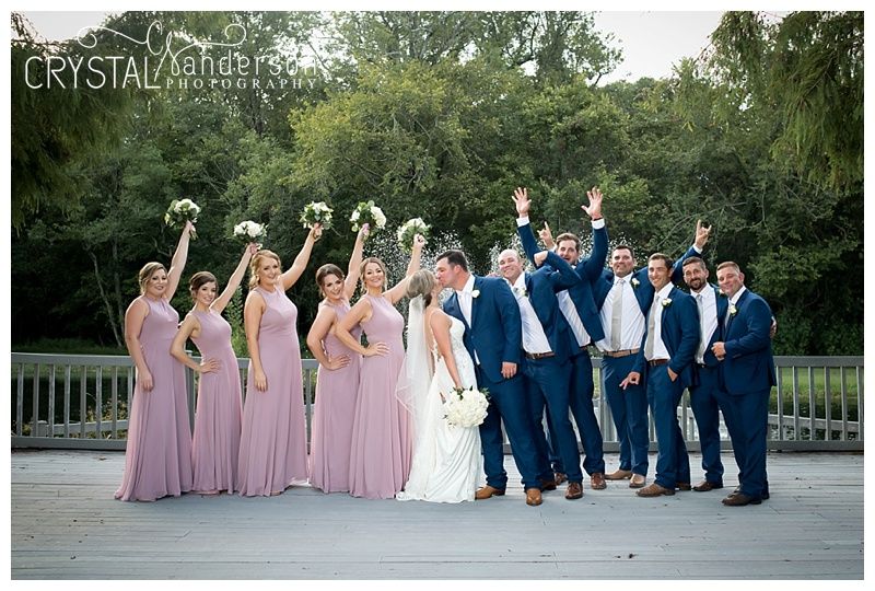 Wedding party in navy suits and lavender dresses poses together on outdoor terrace.