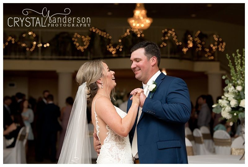 Couple shares romantic dance moment under warm lighting and floral decorations.