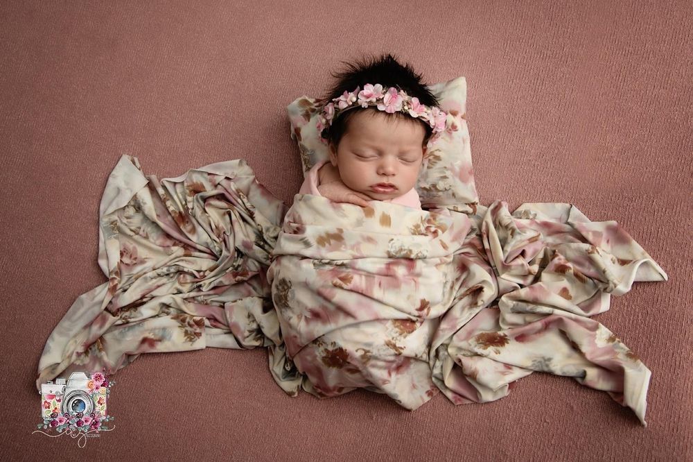 Sleeping newborn posed on pink background with floral wrap and delicate headpiece.