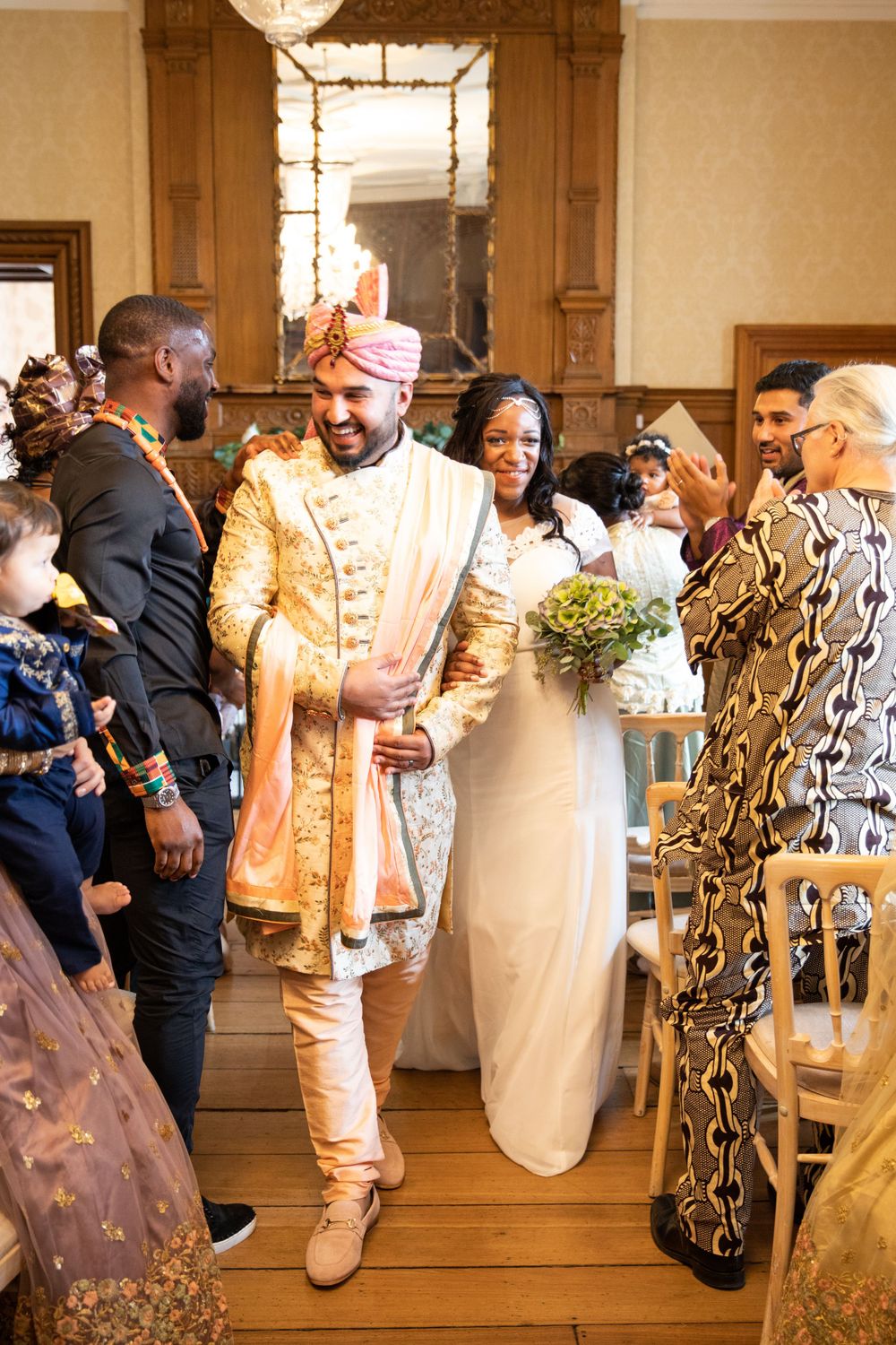 Wedding guests celebrate with the newlyweds in an elegant indoor venue with wooden floors.