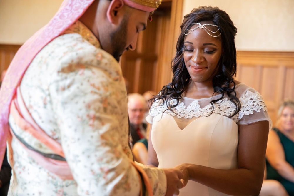 A couple shares a tender moment during their wedding ceremony as they exchange rings in an elegant indoor setting.