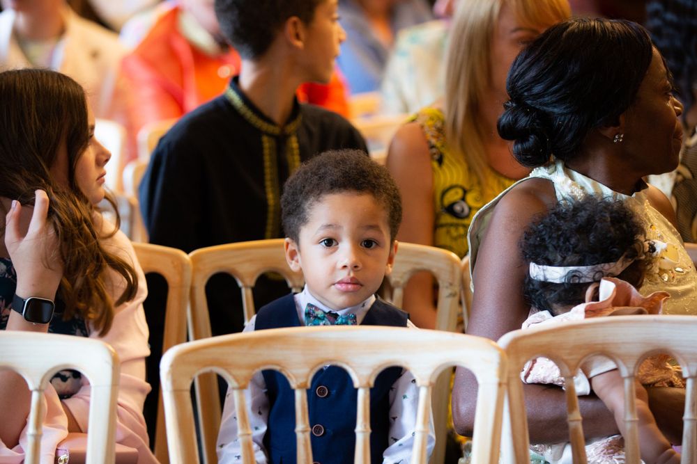 Young wedding guest in formal attire seated among other attendees during ceremony.