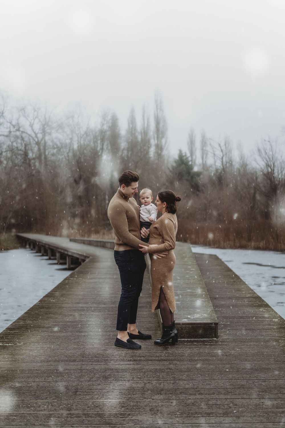 Family sharing an intimate moment on a wooden walkway during light snowfall.