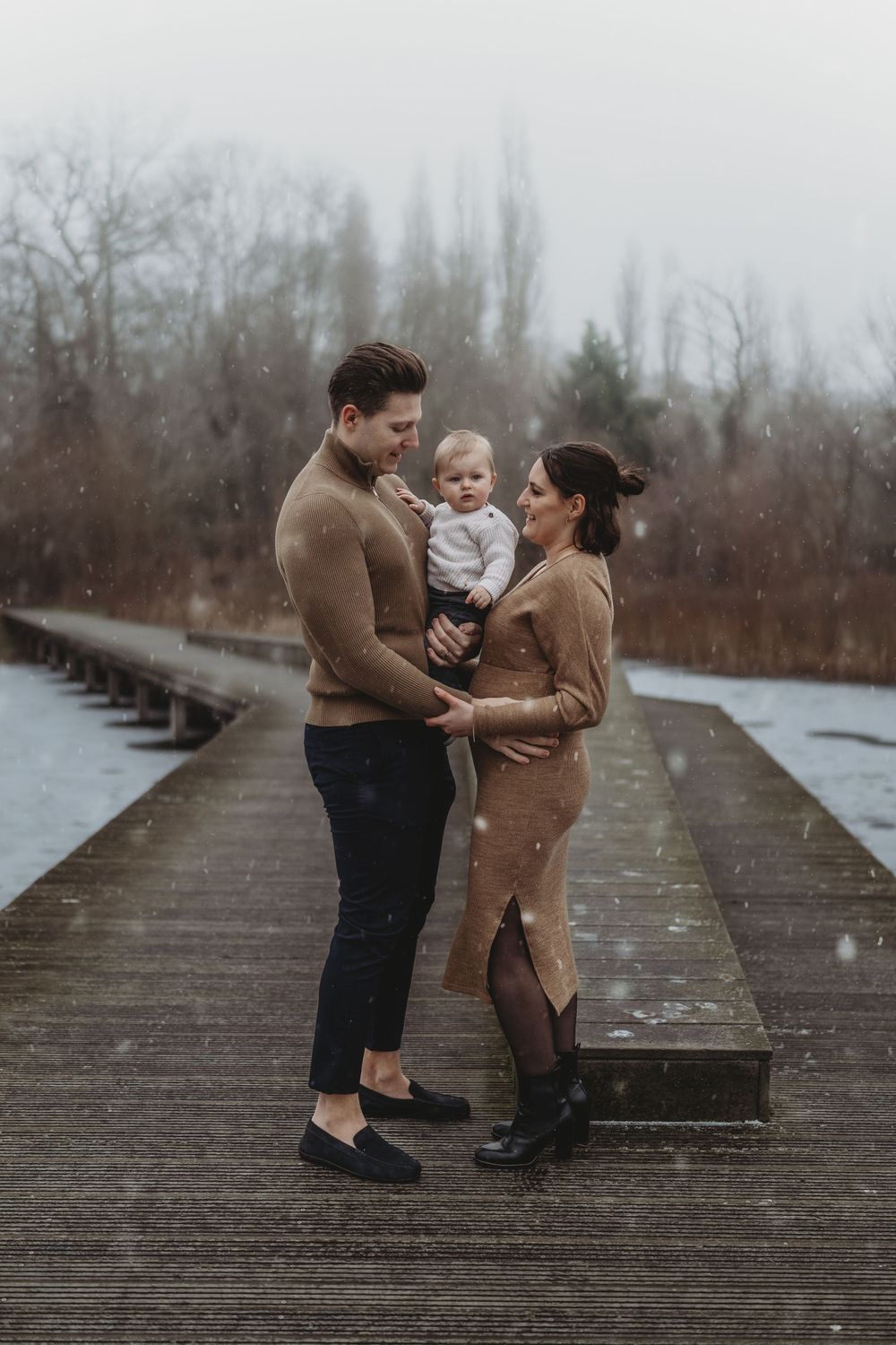 Family of three standing close together on a wooden boardwalk during a winter day.