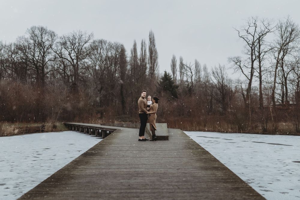 A couple embraces on a wooden boardwalk surrounded by snowy winter landscape and bare trees.