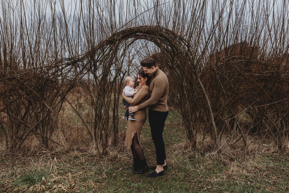 Intimate family moment beneath natural arch of woven branches.