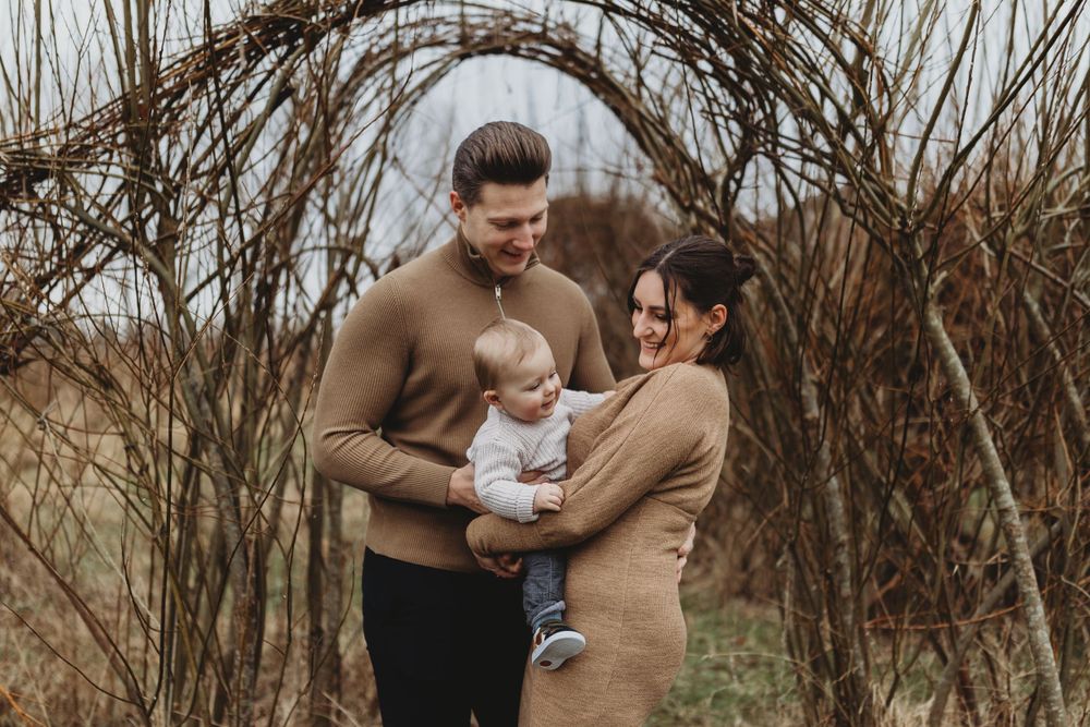 Intimate family gathering under rustic branch archway in earth-toned clothing.