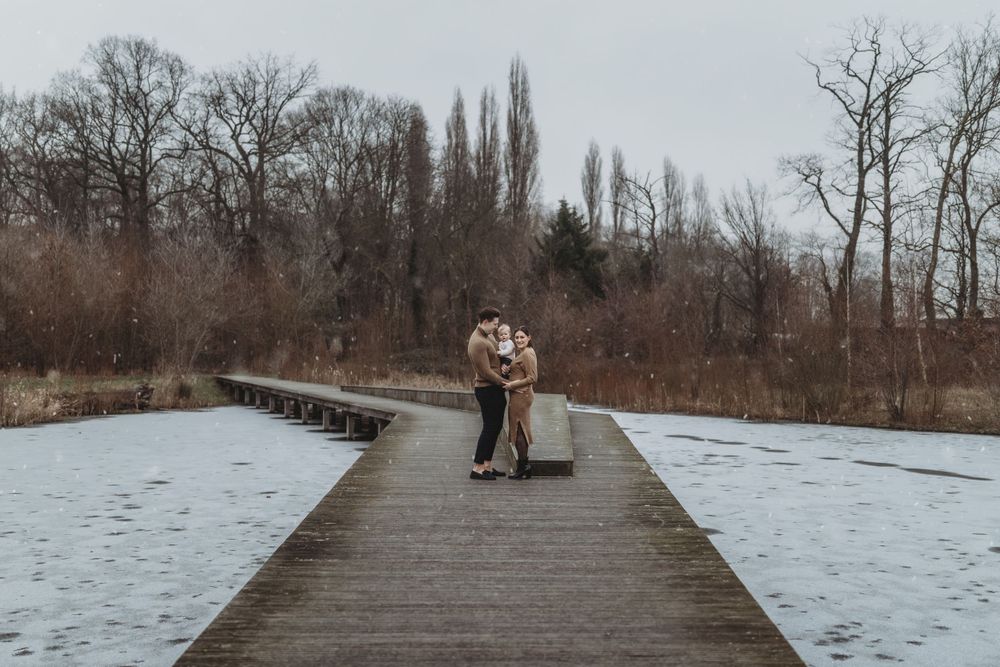 Winter scene of figures on a wooden boardwalk surrounded by snow and bare trees.