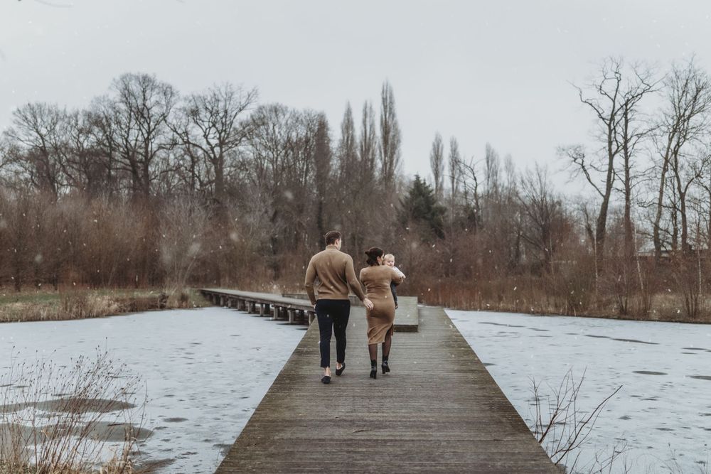 Couple walking hand in hand on a wooden boardwalk surrounded by snowy winter landscape.