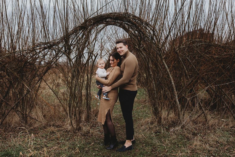 Family portrait under rustic willow arch in autumn landscape.