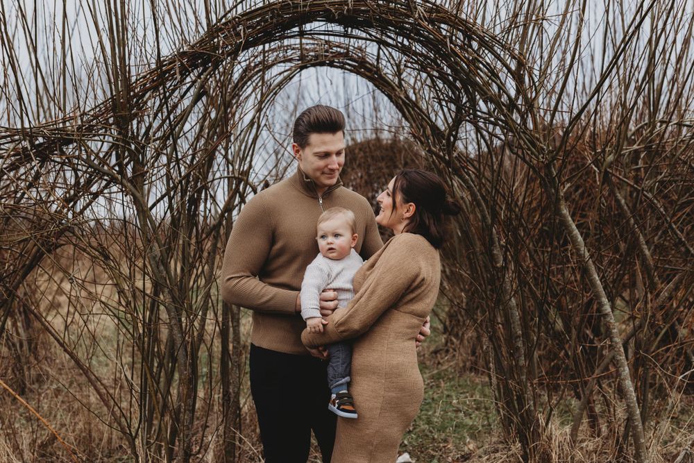 Gentle family moment photographed beneath intertwined winter branches in neutral tones.