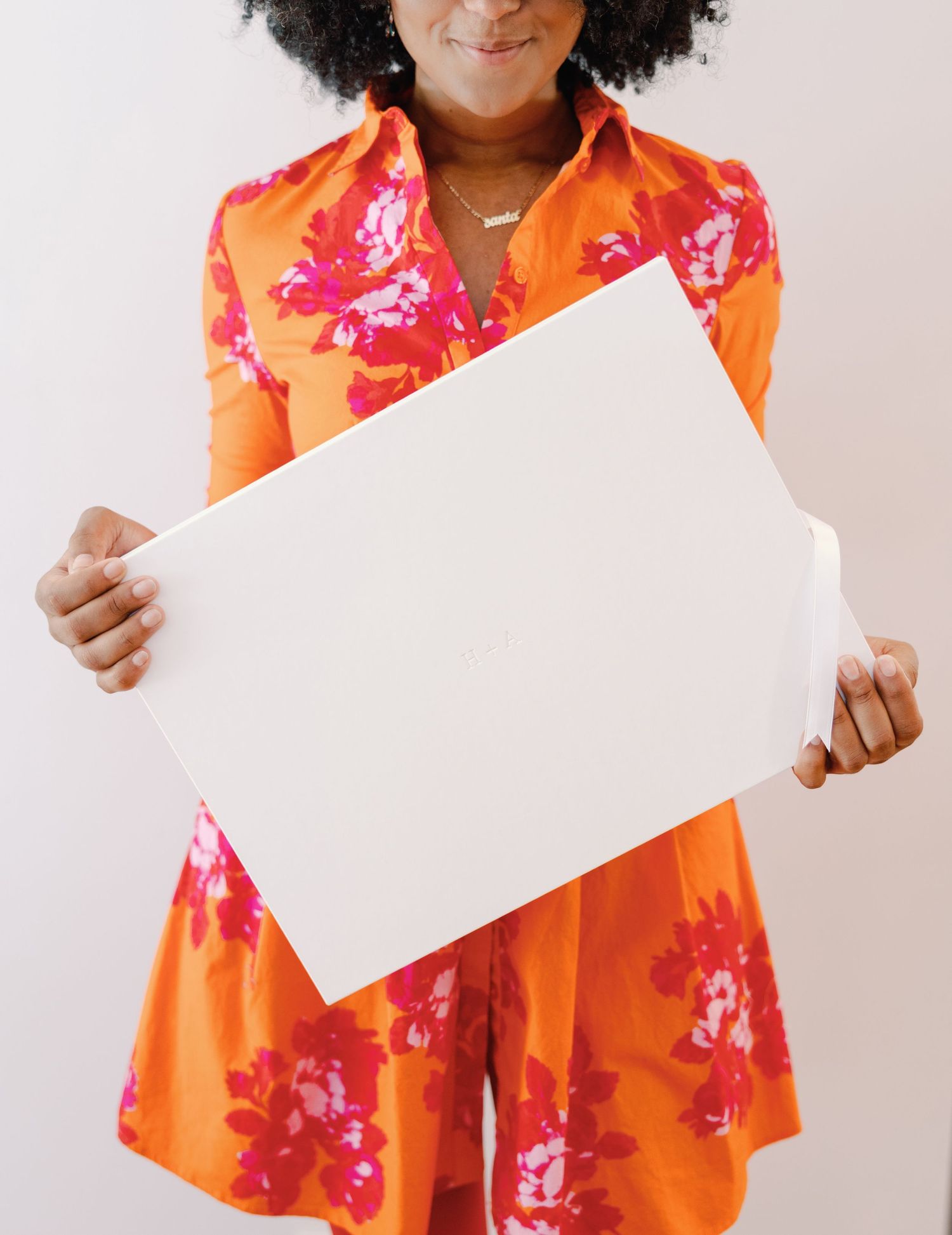 Woman in orange floral dress holding a large white wedding photo album print.
