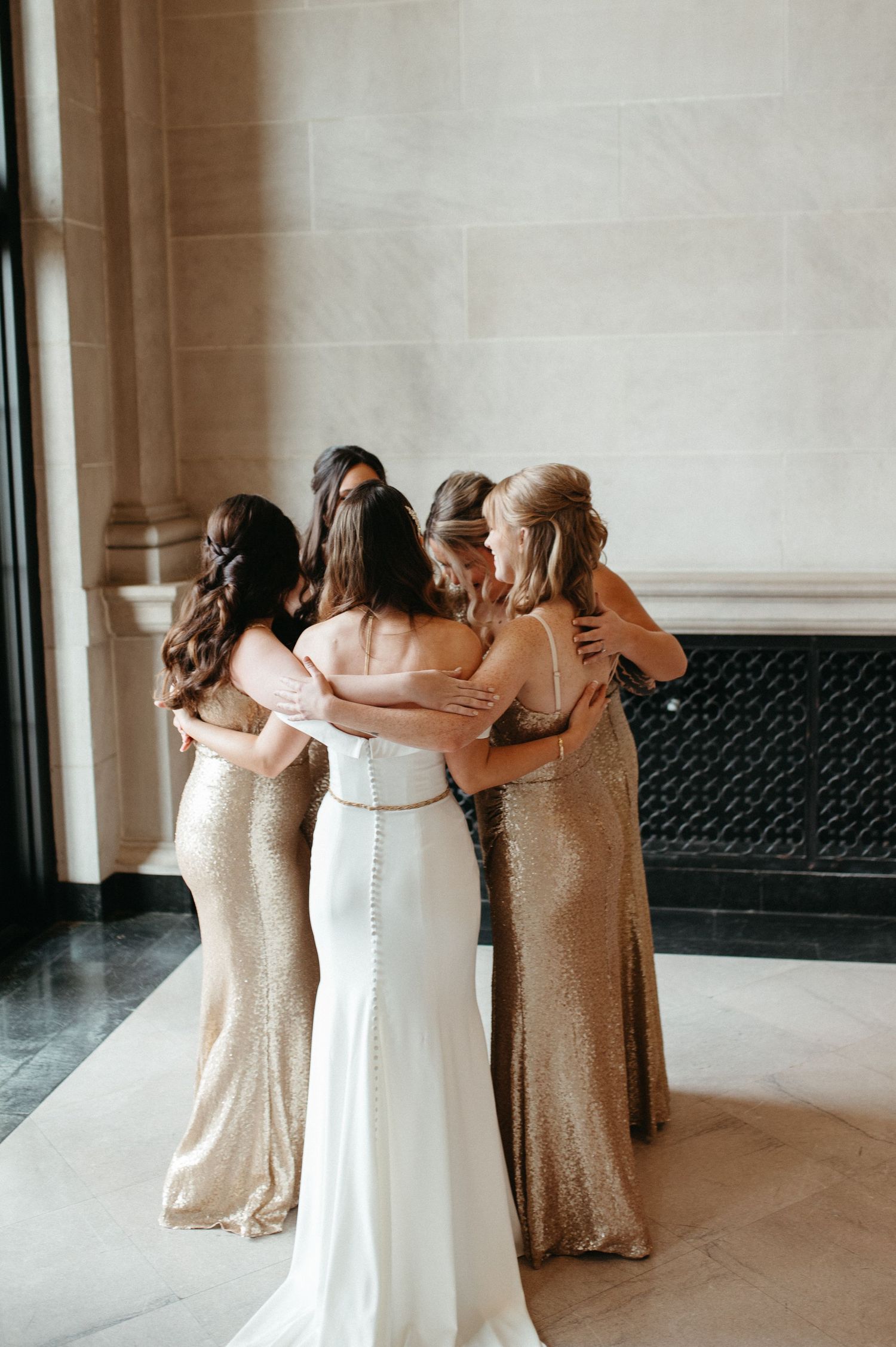 Group huddle showing backs of bridesmaids in gold sequin dresses with bride in white.