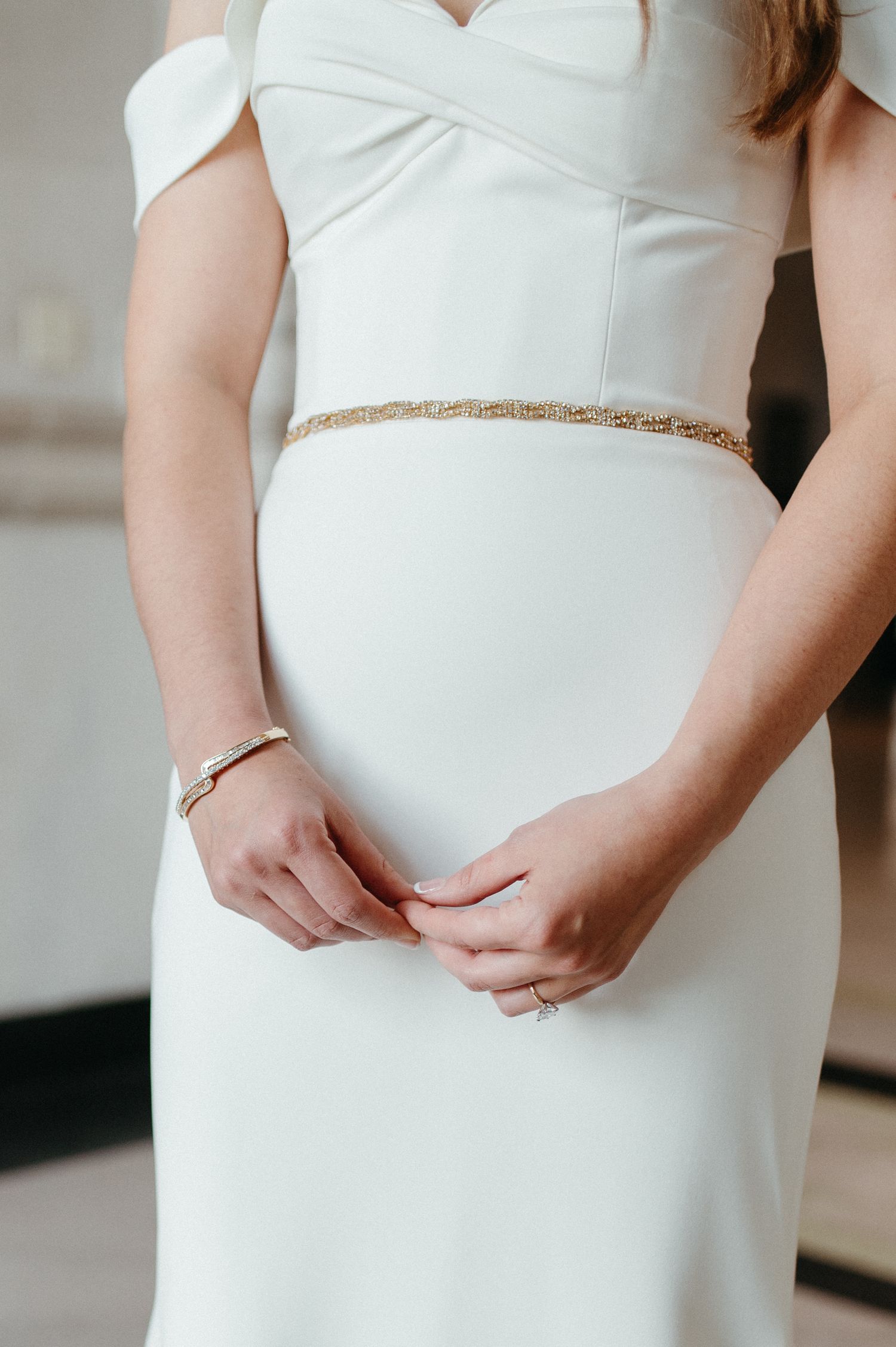 Close-up of white wedding dress with delicate gold belt detail and bracelet.