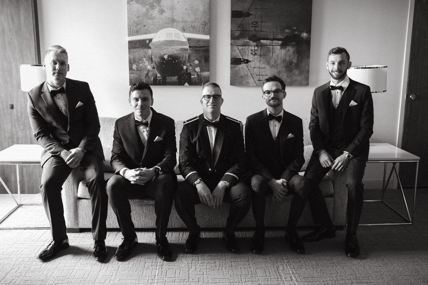 Black and white photo of groomsmen in formal suits sitting on a bench.