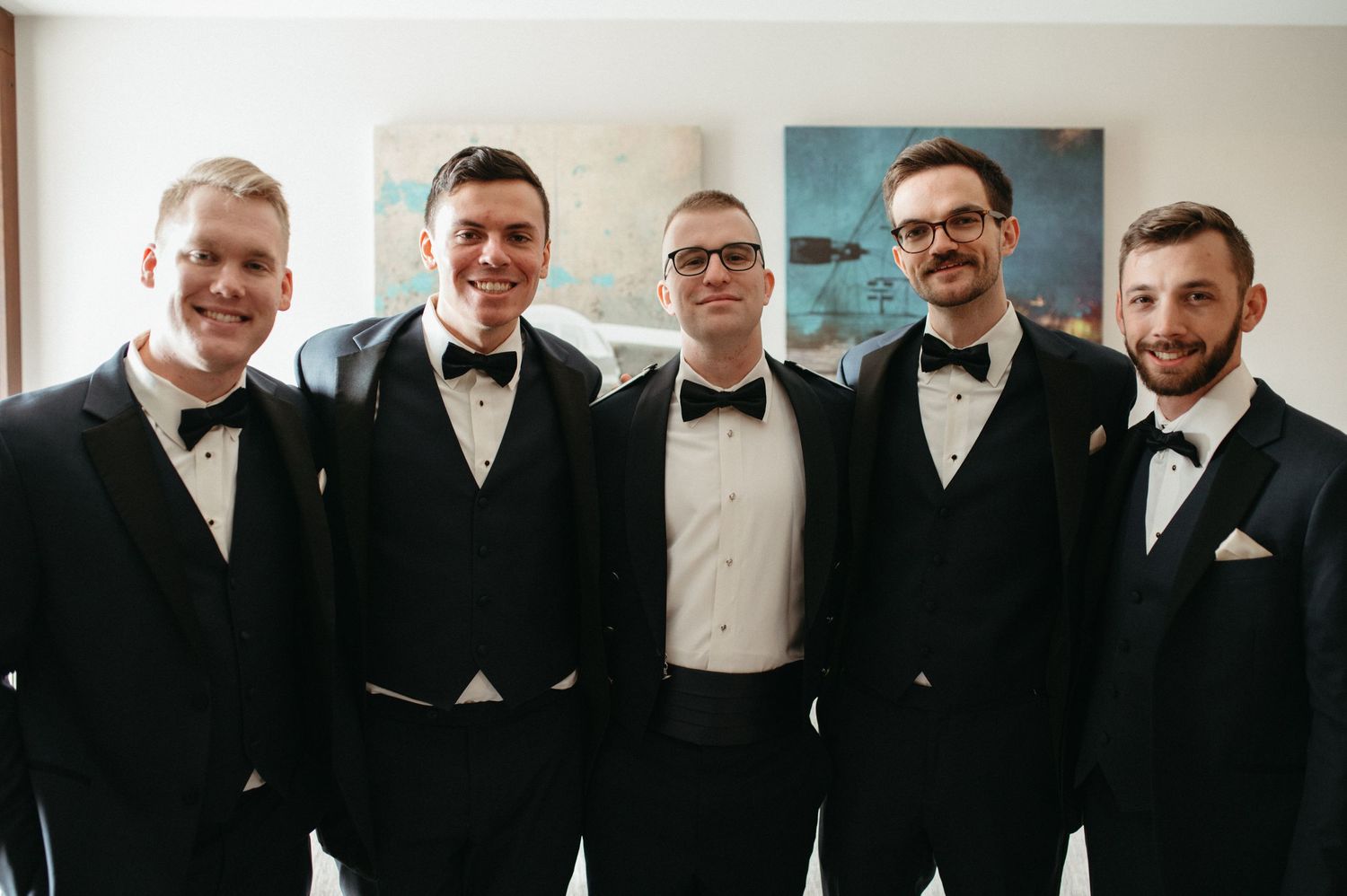 Group portrait of groomsmen in black tuxedos and bowties smiling at camera.