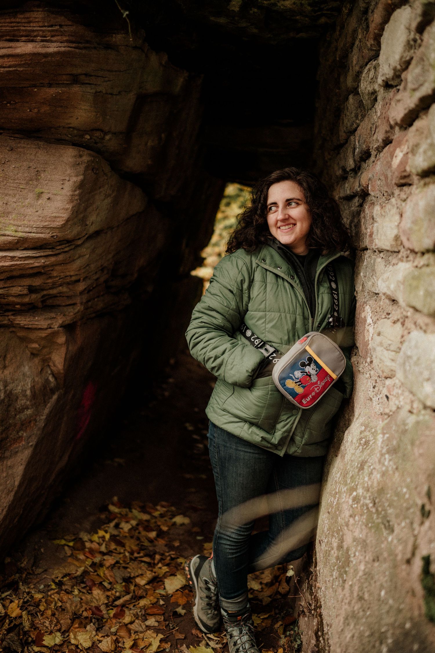 Person exploring a rocky cave formation filled with autumn leaves.