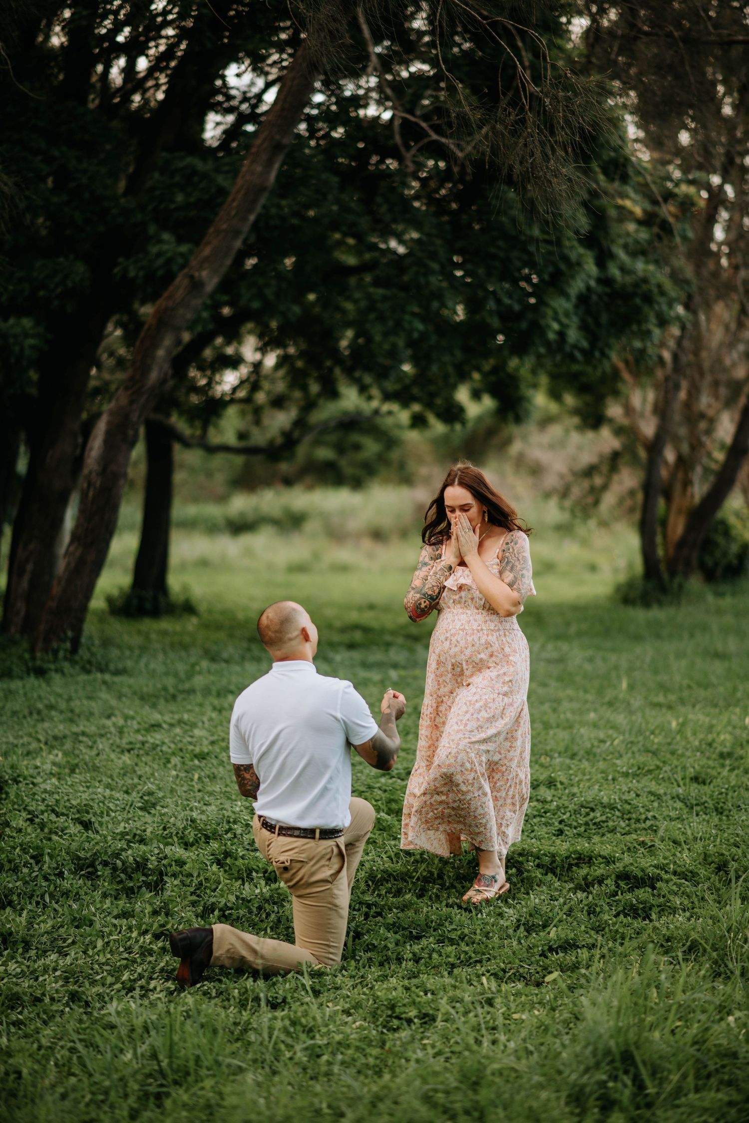 An intimate proposal moment captured in a lush green meadow during golden hour.