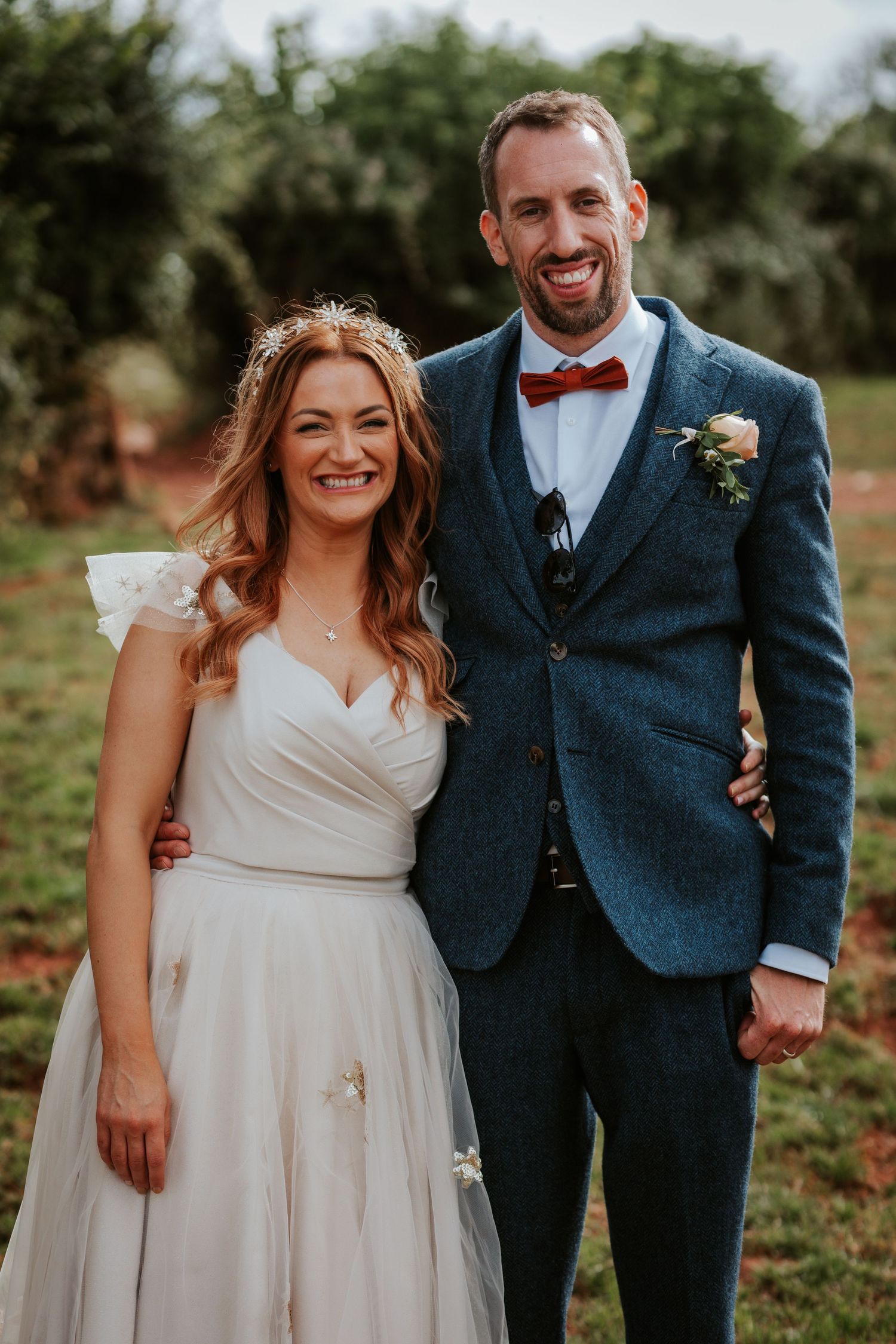 A wedding portrait of a couple in formal attire against a natural outdoor background.