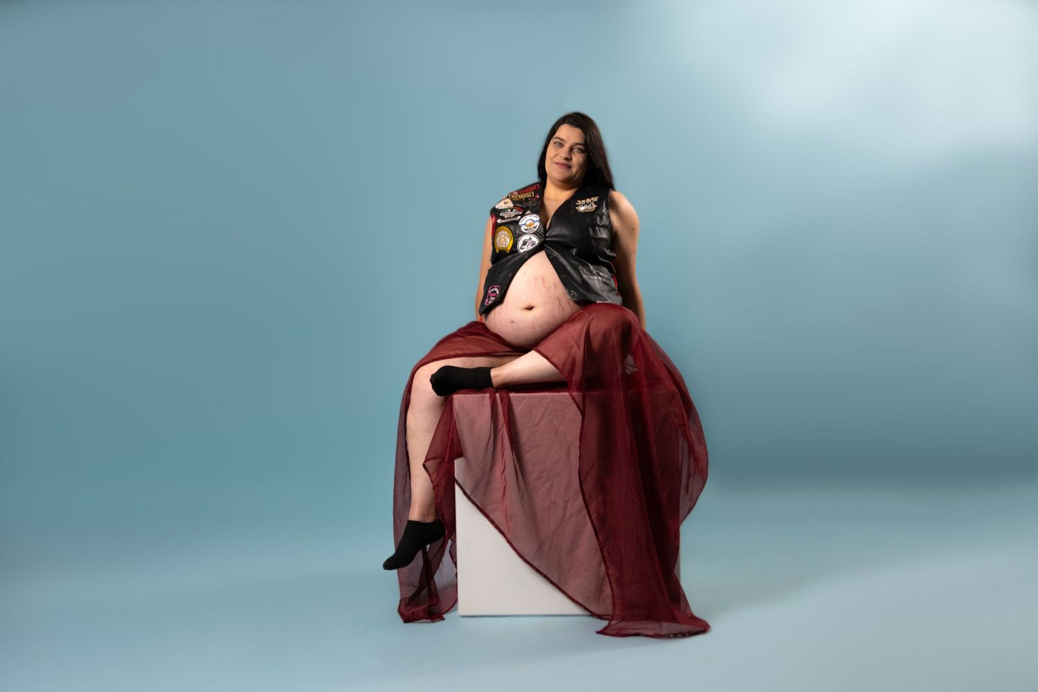 Maternity photo of woman in red flowing dress against blue studio background.