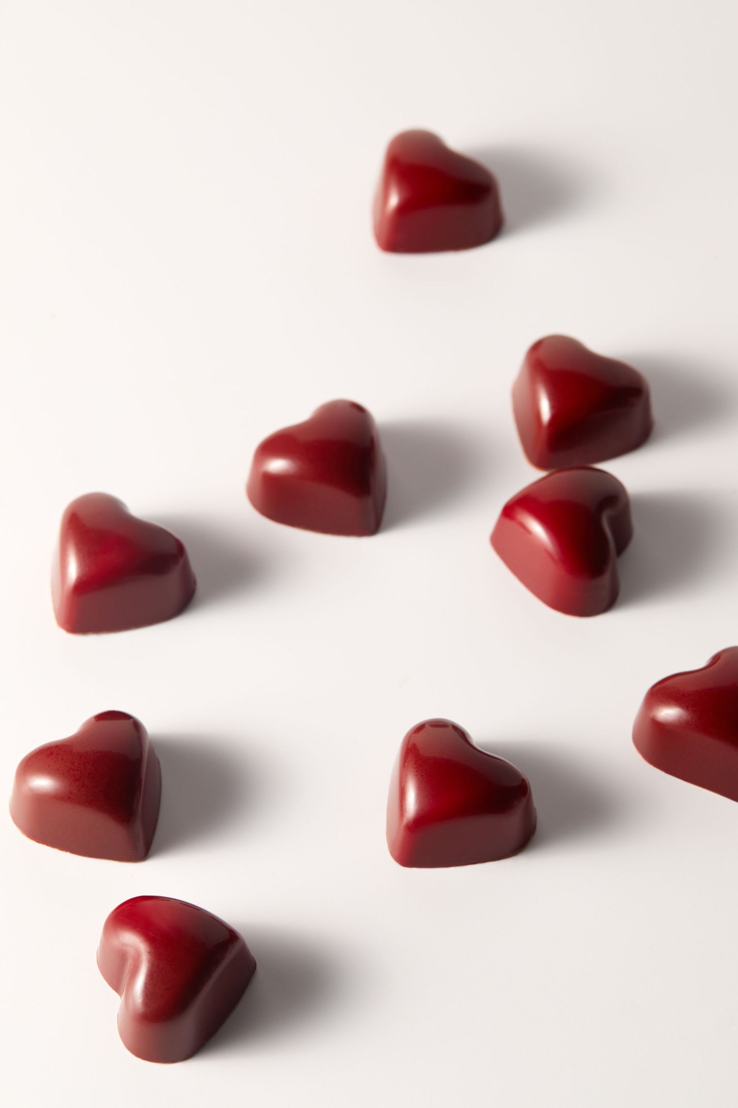 Red heart-shaped chocolate candies arranged on white background.