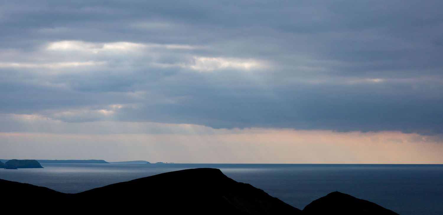 Dramatic seascape with sunbeams breaking through stormy clouds over coastal mountains.