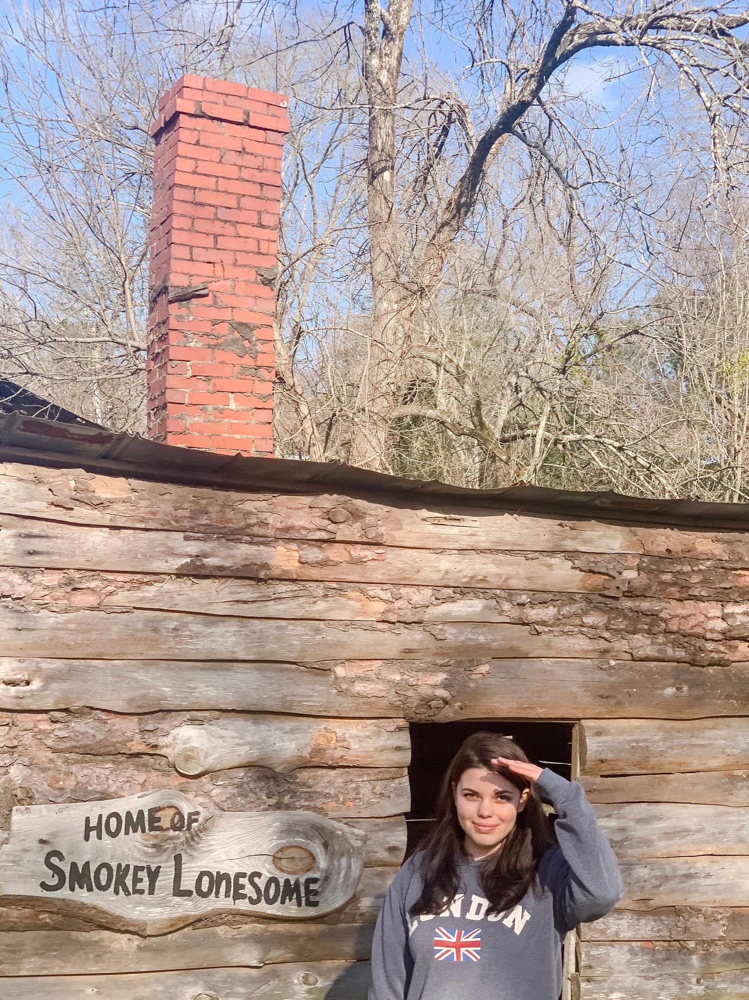 Historic log cabin structure with brick chimney and wooden sign reading 'Smokey Lonesome'.